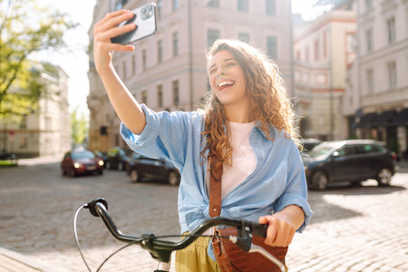 Woman using mobile phone while walking with a bicycle. Selfie time. People, blogging and lifestyle.の写真素材