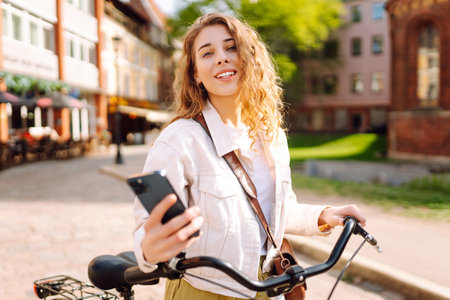 Young woman using mobile phone while riding bicycle at the city street outdoor. Selfie time.の写真素材