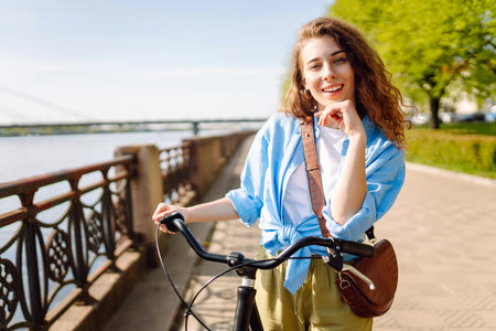 Smiling woman riding bicycle on sidewalk in city spring park. Active urban lifestyle concept.の写真素材