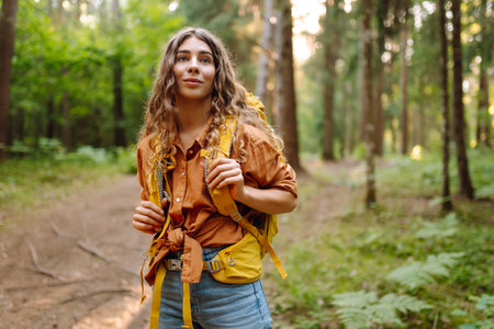 Tourist woman hiking alone in thick autumn forest. Stylish female looks for pathway among trees.の写真素材