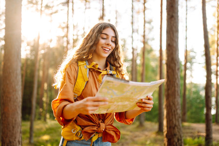A traveler woman stands in a lush forest, examining a map with a focused expressionの写真素材