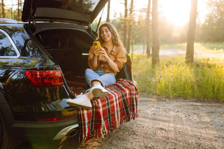 Young woman enjoys a sunny day outdoors while sitting in her car. Travel, weekend, nature, relaxの写真素材