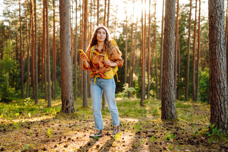 Young woman using mobile application to navigate in autumn forest. Happy tourist trying to find wayの写真素材