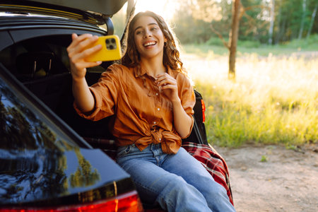 Happy Woman is resting in trunk of car and taking selfie. Selfie time. Lifestyle, travelの写真素材