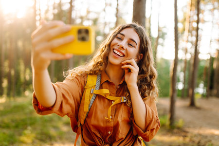 Beautiful woman taking picture of herself while walking in sunny forest. Selfie in nature. Adventureの写真素材