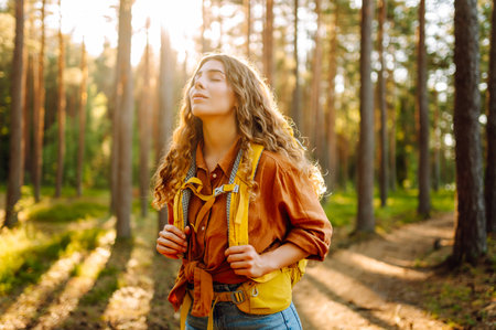 Tourist woman hiking alone in thick autumn forest. Stylish female looks for pathway among trees.の写真素材