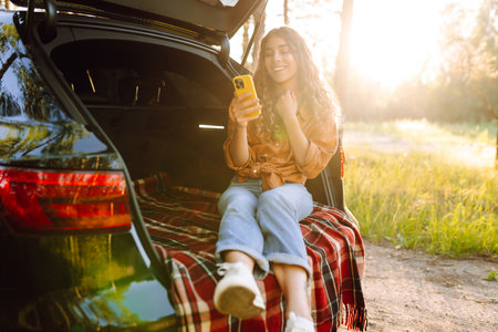 Young woman enjoys a sunny day outdoors while sitting in her car. Travel, weekend, nature, relaxの写真素材
