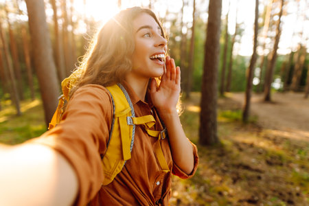Beautiful woman taking picture of herself while walking in sunny forest. Selfie in nature. Adventureの写真素材