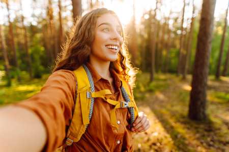 Beautiful woman taking picture of herself while walking in sunny forest. Selfie in nature. Adventureの写真素材