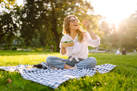 Woman enjoying a poke bowl on sunny day in a park while sitting on a picnic blanket. Concept picnicの写真素材