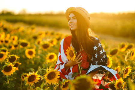 Beautiful girl in hat with the American flag in a sunflower field. 4th of July. Fourth of July....