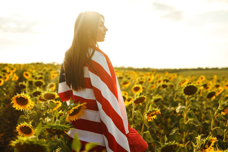 Beautiful girl in hat with the American flag in a sunflower field. 4th of July. Fourth of July. Freedomの写真素材