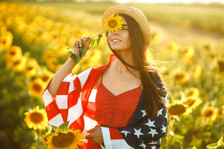 Beautiful girl in hat with the American flag in a sunflower field. 4th of July. Fourth of July. Freedomの写真素材