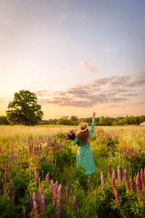 Stylish woman in a straw hat with a bouquet of flowers on a field with lupins. Lifestyle concept.の写真素材