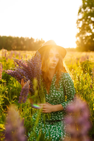 Stylish woman in a straw hat with a bouquet of flowers on a field with lupins. Lifestyle concept.の写真素材