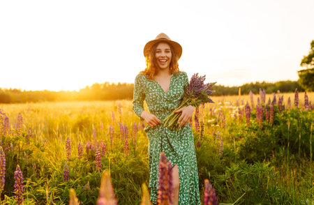 Stylish woman in a straw hat with a bouquet of flowers on a field with lupins. Lifestyle concept.の写真素材