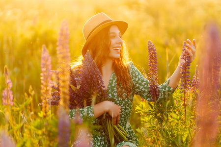Stylish woman in a straw hat with a bouquet of flowers on a field with lupins. Lifestyle concept.の写真素材