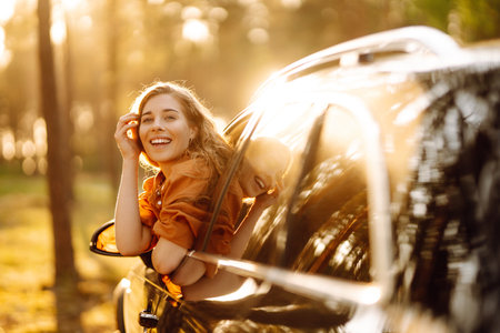 A young woman feels freedom leaning out of a car window in a sunny forest. Travel concept.の写真素材