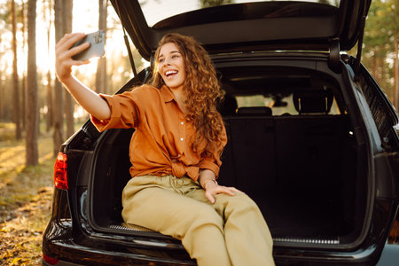 A woman in the trunk of a car at sunset. Traveling by car, camping. Active lifestyle.の写真素材