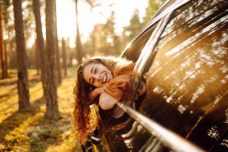 A young woman feels freedom leaning out of a car window in a sunny forest. Travel concept.の写真素材