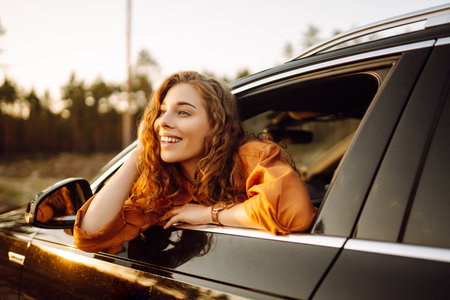 A young woman feels freedom leaning out of a car window in a sunny forest. Travel concept.の写真素材