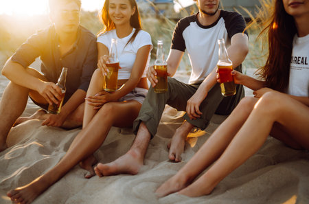 Young people sitting together at beach, drinking beer. Group of friends cheers with beers at the beach.の写真素材