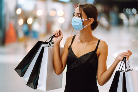 Fashionable woman in protective medical mask with shopping bags walking in the mall. Covid-19.の写真素材
