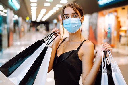 Fashionable woman in protective medical mask with shopping bags walking in the mall. Covid-19.の写真素材
