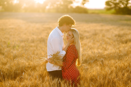 Young happy couple hugging on a wheat field, on the sunset. Enjoying time together.の写真素材