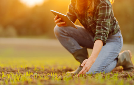 Farmer woman in boots checks the quality of the soil before sowing in her hands with digital tablet.