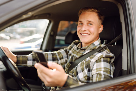 Smiling man using smartphone sitting on driver's seat in car. Car travel, lifestyle concept.