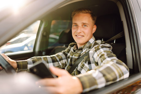 Smiling man using smartphone sitting on driver's seat in car. Car travel, lifestyle concept.