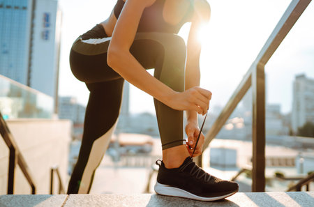 Young woman getting ready for jogging outdoors while lacing her sneakers. Health and sport concept.の写真素材
