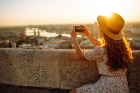 Young Woman on vacation using mobile phone to take photo of sunset of city. Rest, lifestyle concept.の写真素材