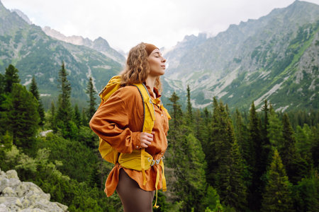 Young traveler woman with a yellow backpack on a cliff. Sports concept, traveler. Active lifestyle.の写真素材