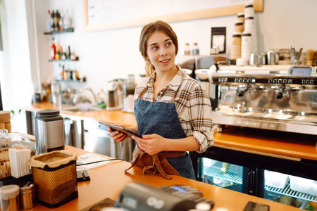 Successful small business owner stands behind counter of coffee shop with digital tablet takes orderの写真素材
