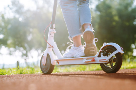 Woman riding electric kick scooter outdoors at sunset, closeup. Ecological transportation concept.の写真素材