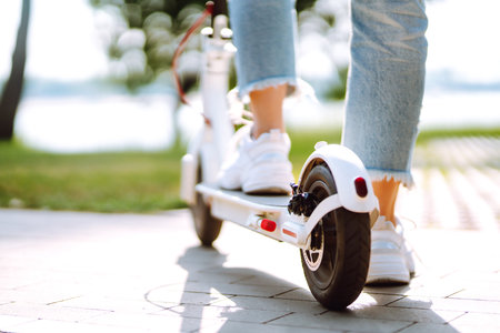 Woman riding electric kick scooter outdoors at sunset, closeup. Ecological transportation concept.の写真素材