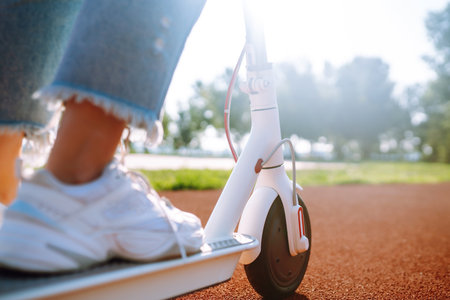 Woman riding electric kick scooter outdoors at sunset, closeup. Ecological transportation concept.の写真素材
