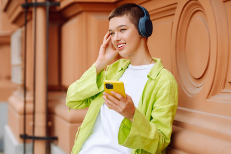 Woman wearing headphones posing outdoors, listens to music and walks along streets of a sunny city.の写真素材