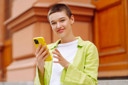 Portrait of woman with short haircut posing on city streets, with phone. Technology, style concept.の写真素材