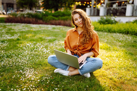 Portrait of a happy woman in sunny park on green lawn with a laptop. Freelance concept, technology.の写真素材