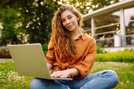Portrait of a happy woman in sunny park on green lawn with a laptop. Freelance concept, technology.の写真素材