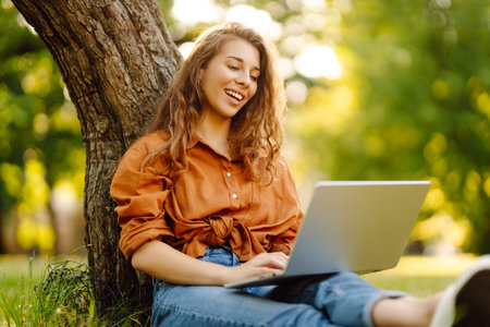 Portrait of a happy woman in sunny park on green lawn with a laptop. Freelance concept, technology.の写真素材