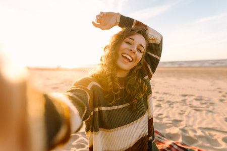 Young woman taking a cheerful selfie on a sandy beach during sunset. Lifestyle, travel, active lifeの写真素材