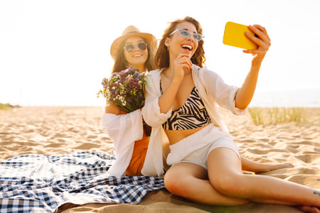 Two pretty friends women making selfie on beach, light and bright summer colors. Friends togetherの写真素材