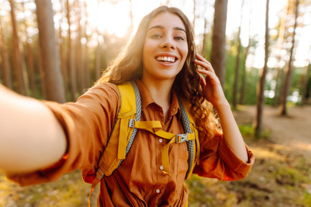 Beautiful woman taking picture of herself while walking in sunny forest. Selfie in nature. Adventureの写真素材