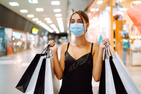 Fashionable woman in protective medical mask with shopping bags walking in the mall. Covid-19.の写真素材