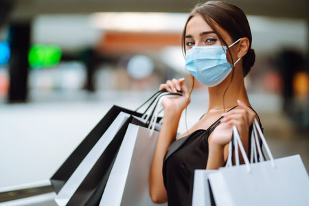 Fashionable woman in protective medical mask with shopping bags walking in the mall. Covid-19.の写真素材