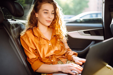 Business beautiful woman with modern laptop sits in back seat of car. Successful startup.の写真素材